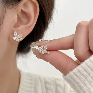 Elegant gold-plated butterfly stud earrings with zircon crystals shown in-ear and hand