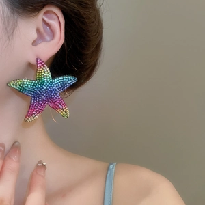Close-up of a large starfish earring with rainbow gradient rhinestones worn by a model