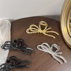 Elegant metal bow hair claws in gold, silver and black finishes on a dark surface