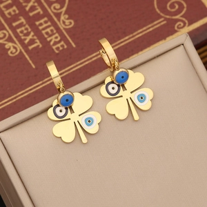 Golden clover earrings with evil eye motif displayed on a vintage book and jewelry box