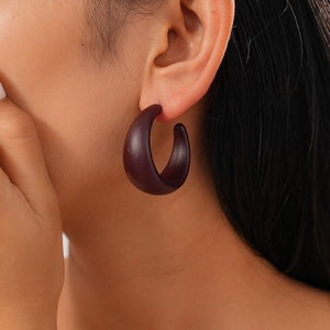 Close-up of matte dark purple acrylic C-shape hoop earrings on a model's ear