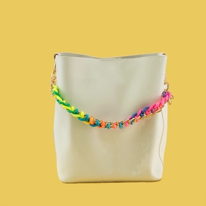 White bucket bag with colorful woven handle and gold metal chain on yellow background