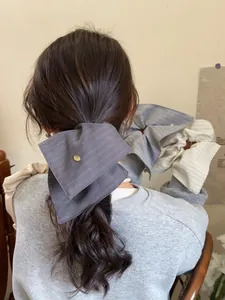 Detail of oversized striped bow hair scrunchie with a central golden metal button