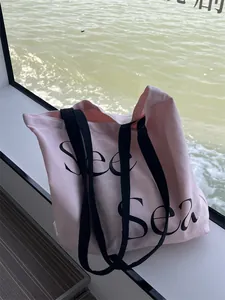 Close-up of pink canvas tote bag with black wide straps and artistic Sea lettering