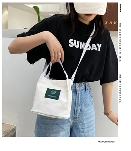Close-up of white canvas bucket bag with green label showing Living Traveling Share text