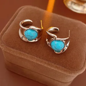 Vintage silver C-shaped hoop earrings with turquoise stones on a brown velvet jewelry box