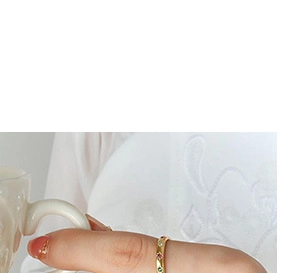Primer plano de un anillo dorado con gemas de colores en la mano junto a una taza