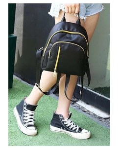 Detail of black nylon backpack featuring contrast yellow zippers and multi-pocket design