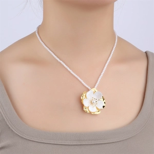 Close-up of gold flower pendant on white pearl necklace worn by a fashion model