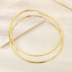 Close-up of two layered gold snake chain necklaces on a textured stone and silk backdrop