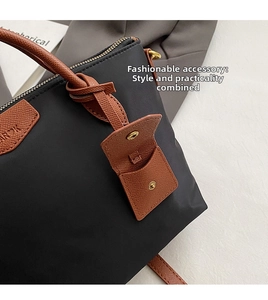 Close-up of black nylon tote bag with brown leather snap-button charm and gold hardware