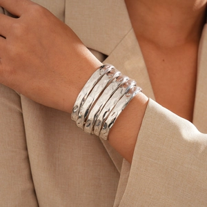 Détail de cinq bracelets argentés à texture martelée sur le poignet d'un mannequin