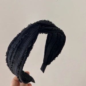 Close-up of black textured fabric headband with cross knot detail held by hand
