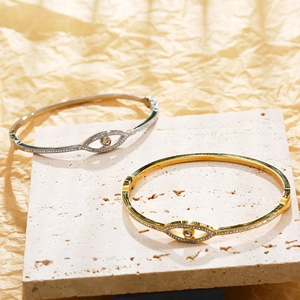Polished 18K gold and silver evil eye bangles with marquise-cut crystals on marble