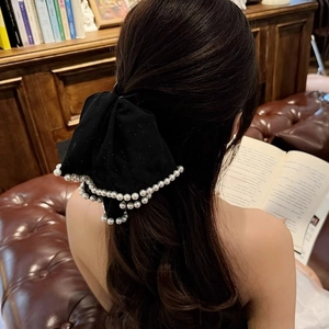 Elegant black velvet bow hair clip with white pearls worn by a model in a retro study room