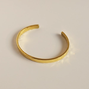 Close-up of golden open bangle with moon surface hammer texture in 18K gold plated steel