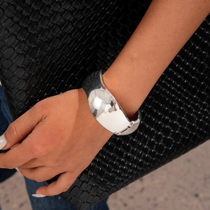 Polished silver wide resin bangle on wrist styled with a luxury woven leather bag