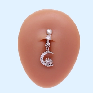 Macro shot of a silver navel ring with star and moon pendants on a silicone model