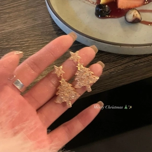 Close-up of hand holding golden Christmas tree earrings with star details and textures