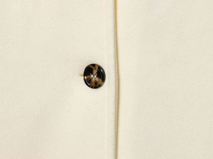 Macro detail of creamy white wool fabric with a dark brown tortoiseshell button