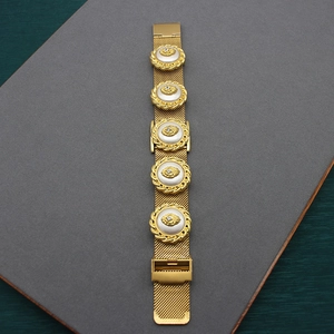 Close-up of gold mesh bracelet featuring white round charms with rhinestone details