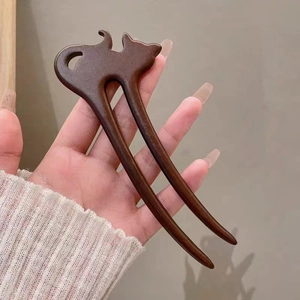 Close-up of deep brown wooden hair pin with a cat-shaped carving and double-prong design
