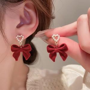 Dettaglio orecchini a fiocco floccato rosso vino con cuore di perla sulla modella