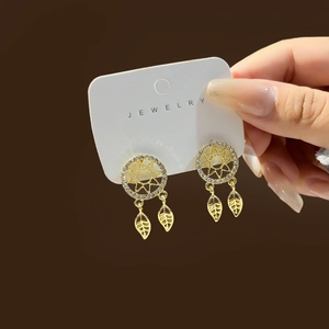 Close-up of golden dreamcatcher earrings with sparkling rhinestones and hollow leaf pendants