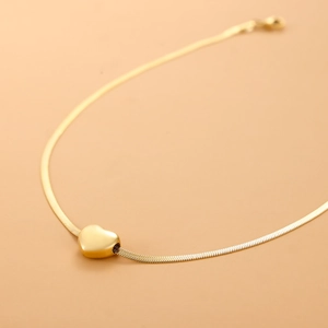 Macro shot of polished gold-plated heart pendant on a smooth snake chain necklace