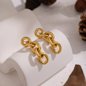 Boucles d'oreilles chaîne en acier inoxydable doré sur un support incurvé blanc