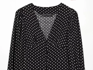 Dettaglio di un abito nero a maniche lunghe con pois bianchi, scollo a V profondo e bottoni
