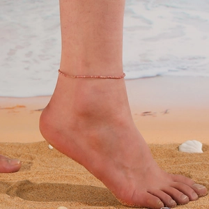 Close-up of a pink beaded crystal anklet worn on the ankle with beach sand background