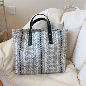 Detail of floral printed tote bag with elegant blue lace patterns and black leather handles