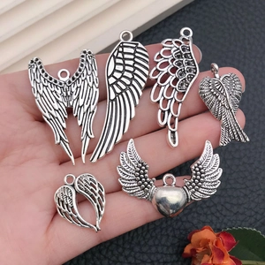 Hand holding six diverse antique silver wing pendants with detailed feather and heart designs