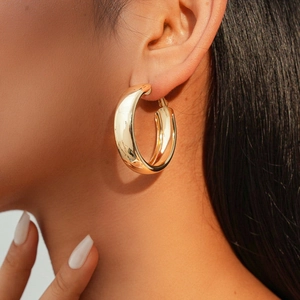 Close-up of a model wearing thick golden metallic hoop earrings with a polished finish