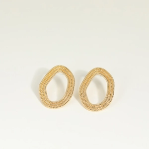 Pendientes de aro dorados geométricos irregulares con textura tejida sobre fondo beige
