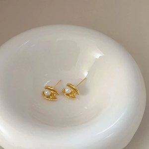 Detail shot of golden shell stud earrings with white pearls in a white ceramic dish