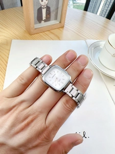 Close-up of a silver square quartz watch with metal strap worn on a woman's wrist