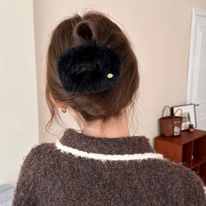 Detail of a black plush hair clip on a model's hair in a cozy home setting