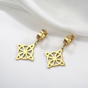 Detail shot of golden Celtic knot earrings resting on elegant white silk fabric