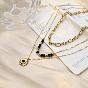 Three-layer gold sun pendant necklace with black beads and chunky chain on white silk