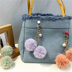 Detalle de pompones de peluche en bolso vaquero con asas de cuero y cadena de perlas