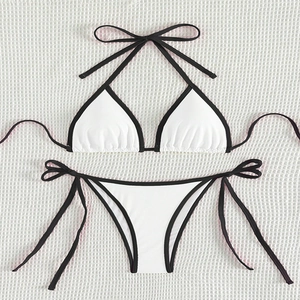 Detail of white bikini with black trim showing side ties and high-stretch fabric texture