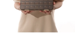 Handheld view of a large brown transparent 21-compartment pill organizer for weekly storage