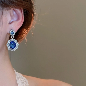 Close-up of elegant blue oval gemstone earrings with sparkling diamond accents on model
