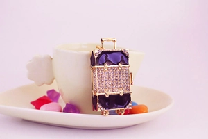 Close-up of diamond-encrusted suitcase keychain with gold trim and rhinestones on white cup