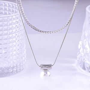 Double-layer silver necklace with cylindrical pendant and white pearl over textured glass