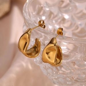 Close-up of gold geometric earrings hanging on a textured glass bowl with a soft pink background