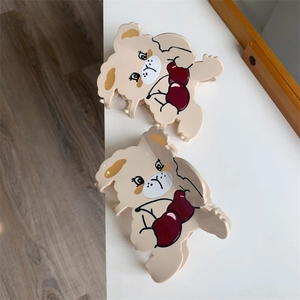 Close-up of beige dog-shaped hair claws with red heart pattern on white background