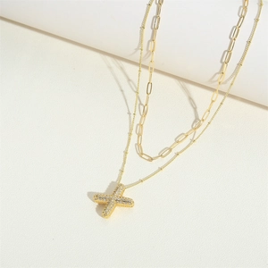 Detail of layered gold necklace with paperclip chain and diamond-set X shaped pendant